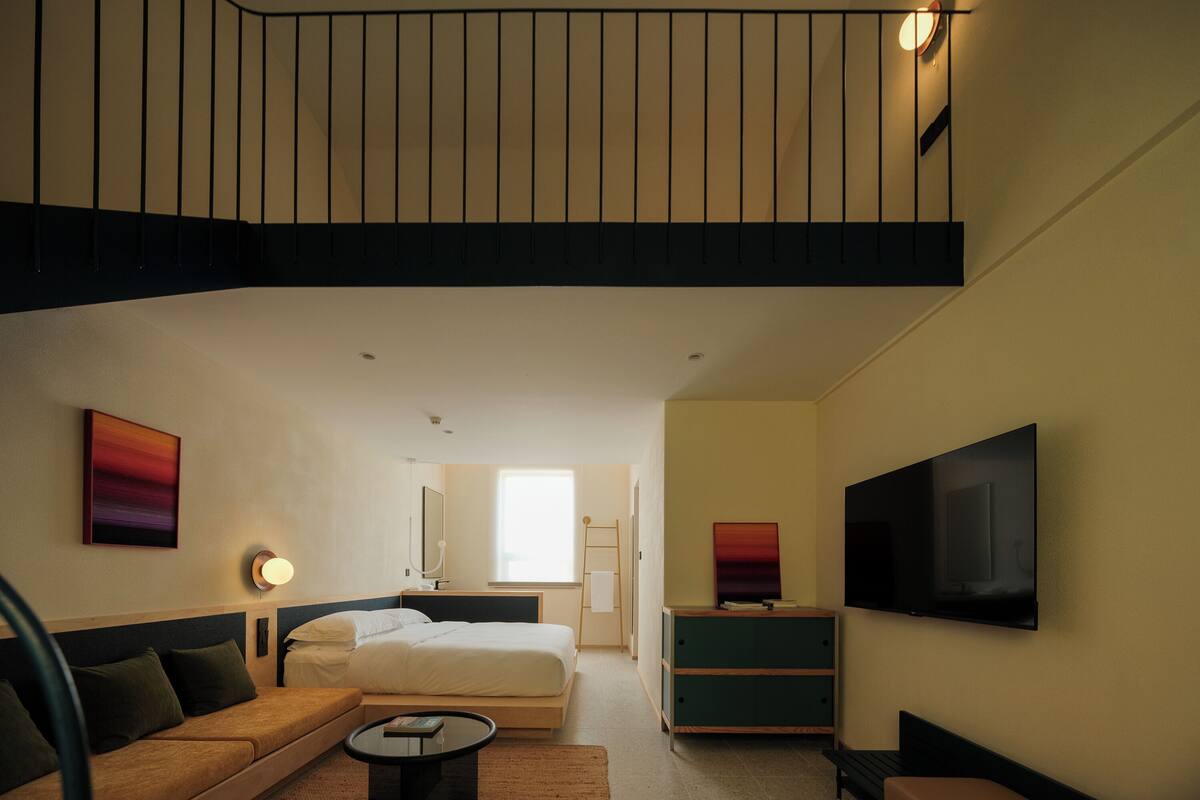 A modern hotel room with a bed, sofa, TV, and a staircase.