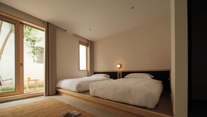 Un dormitorio moderno con dos camas, un amplio ventanal corredero que da a un balcón y una pequeña mesa con una silla afuera.