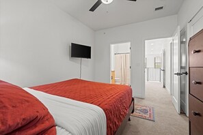 A bedroom with a bed, a television, a wardrobe, and a hallway leading to another room.