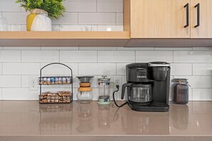 A kitchen with a Keurig coffee maker, a coffee grinder, a jar of coffee, and a plant on the counter.