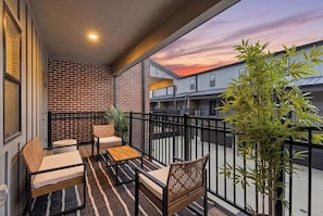 A balcony with seating, a potted plant, and a view of buildings.