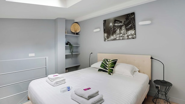 Ein modernes Hotelzimmer mit Bett, Nachttischen, einem Wandregal mit Dekoration und einem Stadtbild.
