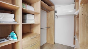 Ein begehbarer Kleiderschrank mit Holzböden, Schubladen und Kleiderstangen, mit ordentlich gefalteter Bettwäsche und einem blauen Bügeleisen.