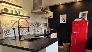A modern kitchen with a central island, bar stools, a red refrigerator, and a black wall with framed pictures.