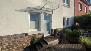 A house with a stone foundation, a wooden deck, and a small outdoor seating area with chairs and planters.