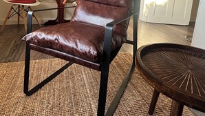 A leather lounge chair with a metal frame, a woven rug, a small round table, and a white chair.