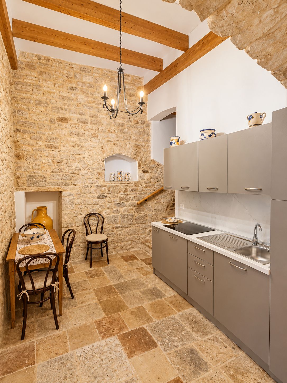 Una cocina rústica con paredes de piedra, vigas de madera, una mesa de comedor con sillas y un lavamanos empotrado.