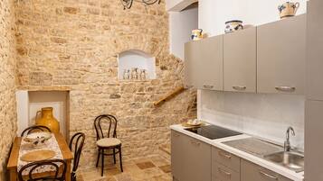 Una cocina rústica con paredes de piedra, vigas de madera, una mesa de comedor con sillas y un lavamanos empotrado.