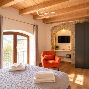 A bedroom with a bed, a chair, a TV, and a stone wall. - PALAZZO RIZZI DIMORA DEI TEMPLARI (Bitetto)