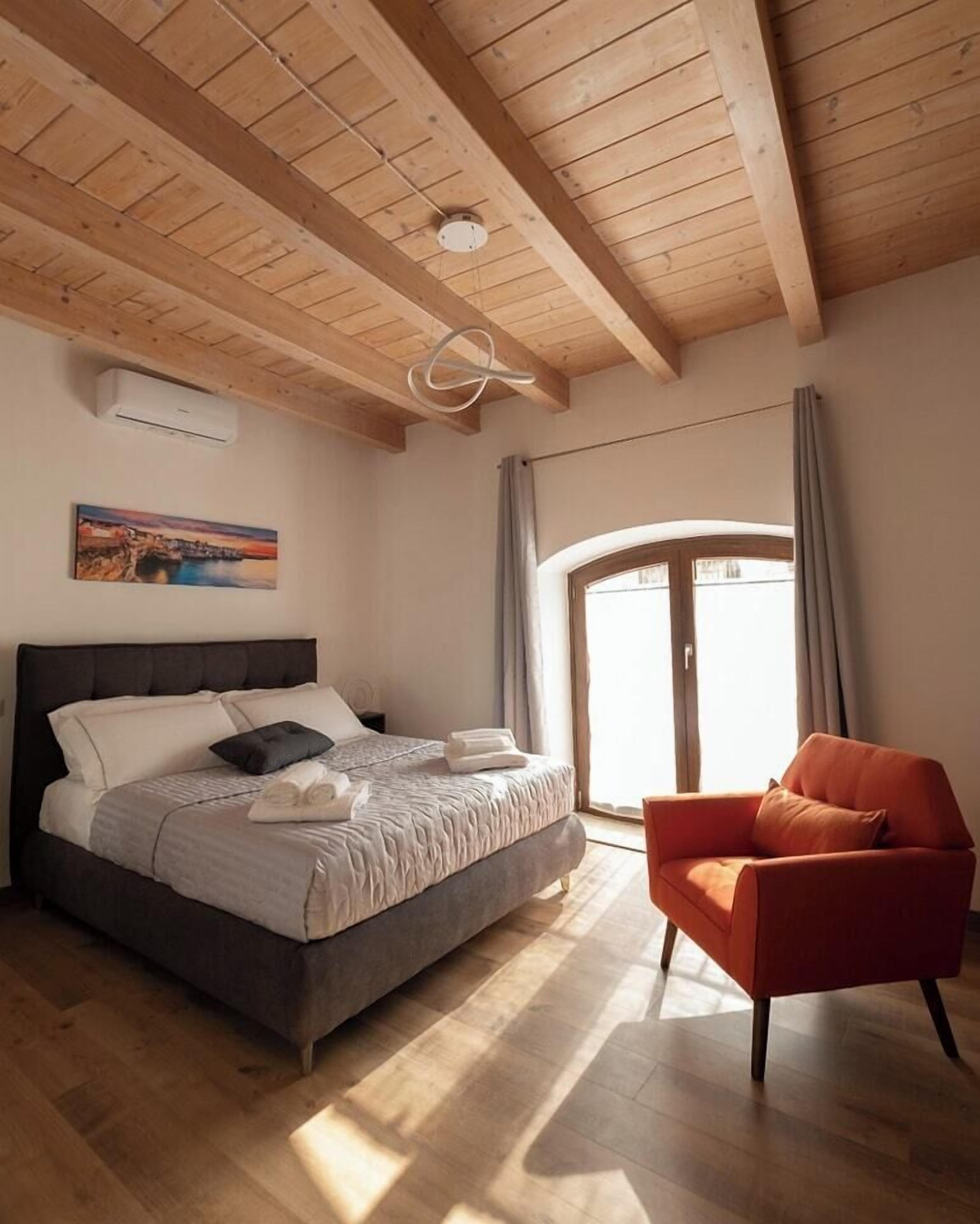 A bedroom with a bed, a chair, a window, and a painting on the wall.