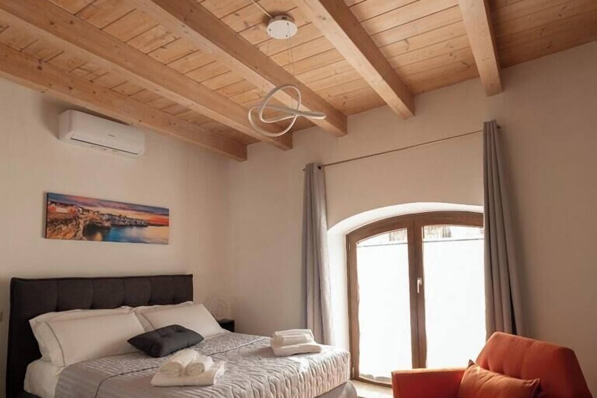 A bedroom with a bed, a chair, a window, and a painting on the wall.