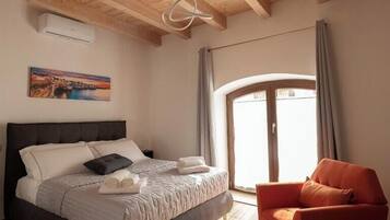 A bedroom with a bed, a chair, a window, and a painting on the wall.