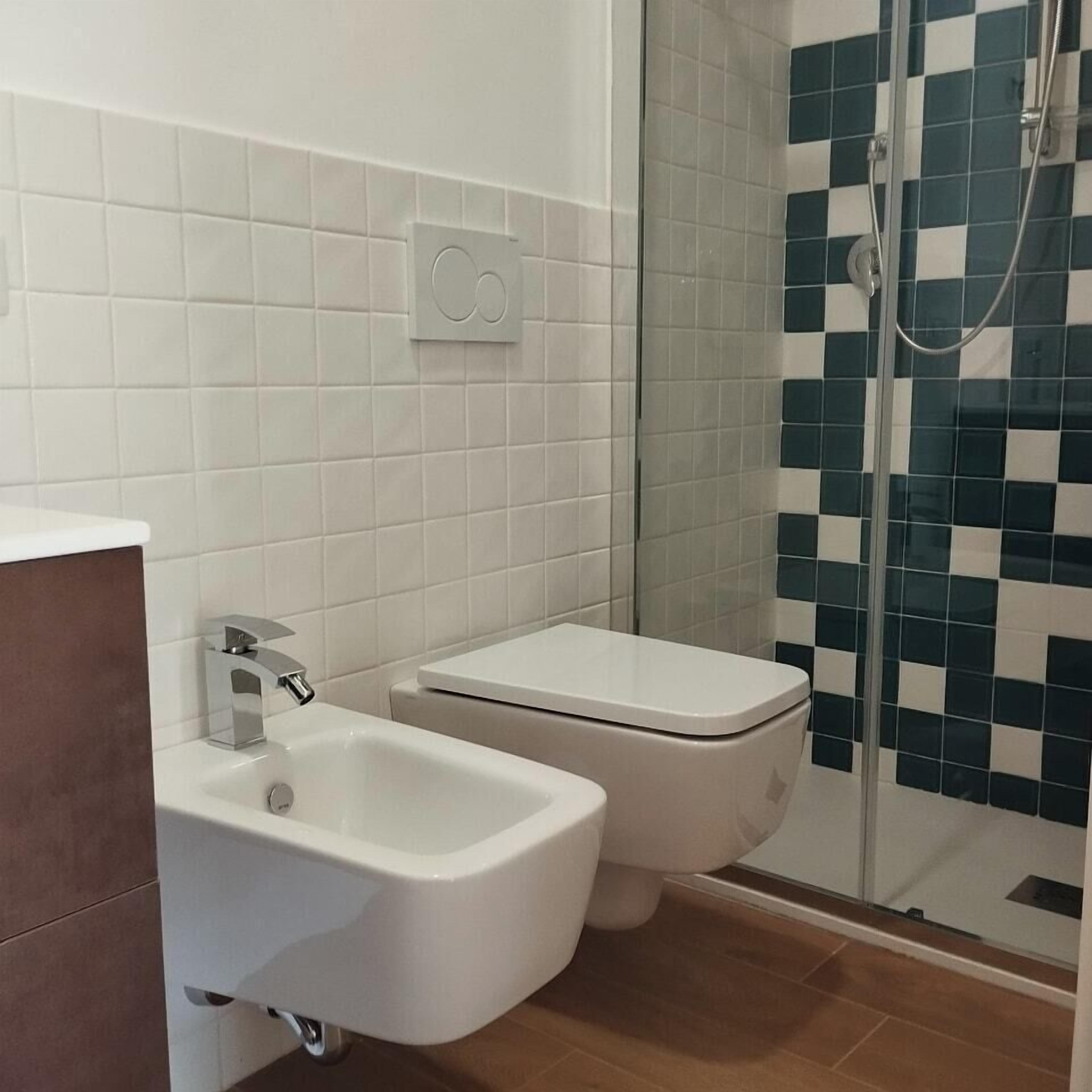 Une salle de bain avec un lavabo blanc, des toilettes et une douche dont le mur est recouvert de carreaux à motifs.