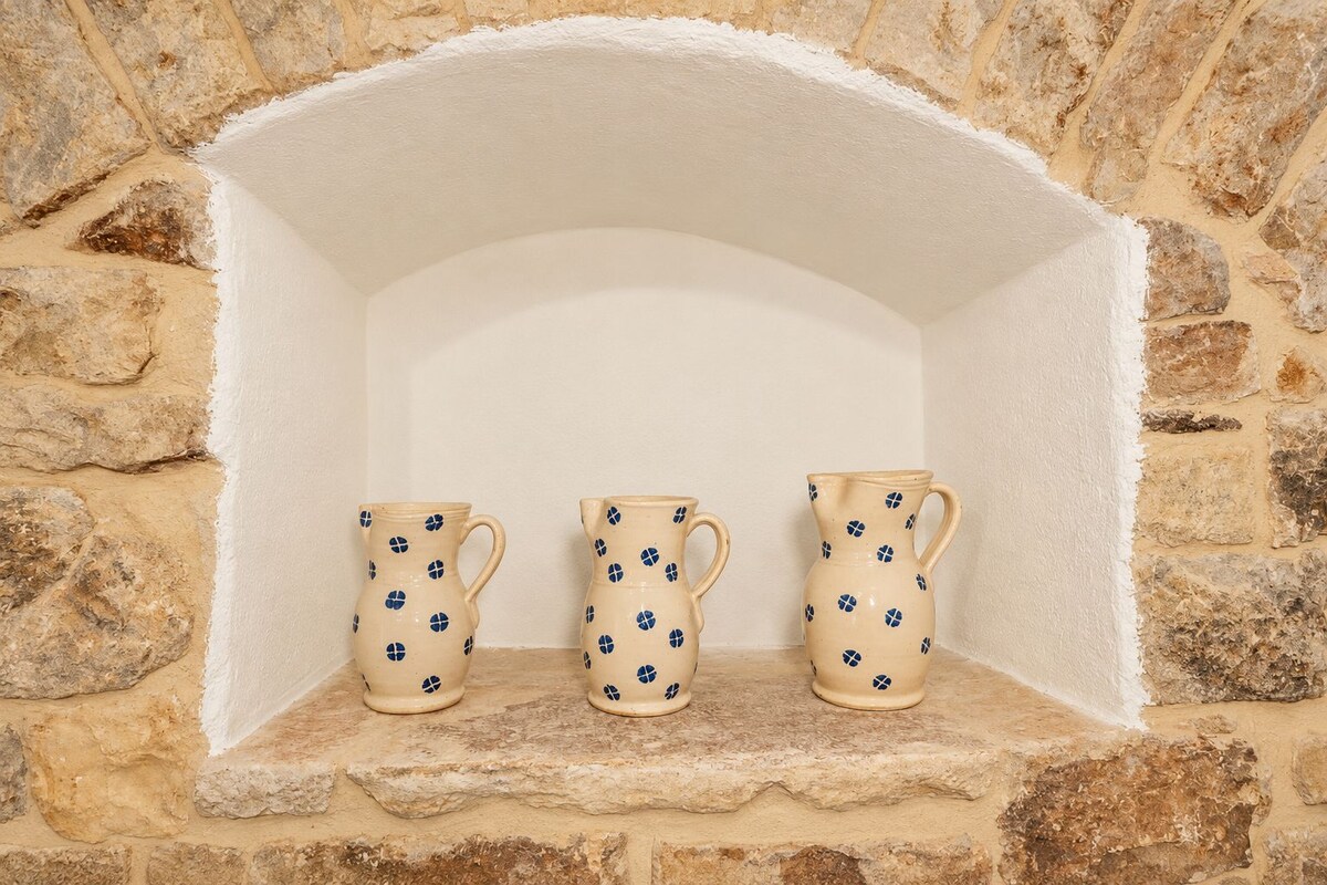 Three ceramic pitchers with a blue pattern, placed on a stone shelf against a stone wall.