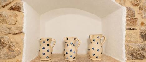Three ceramic pitchers with a blue pattern, placed on a stone shelf against a stone wall.