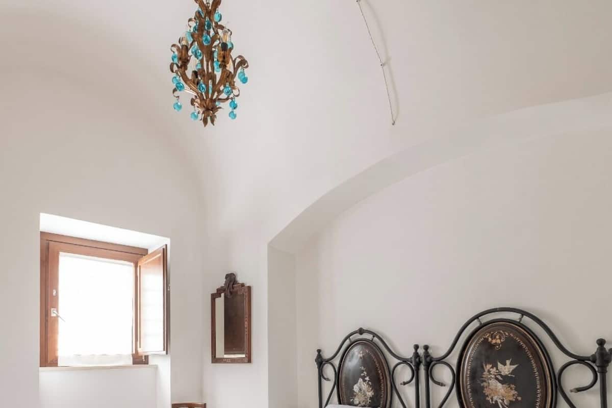 A bedroom with a large bed, a chandelier, a window, and a mirror.