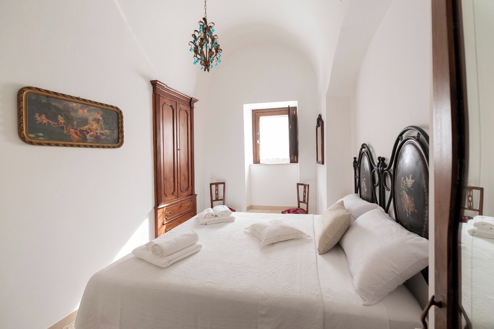 A bedroom with a bed, a wooden wardrobe, a chandelier, and a window.