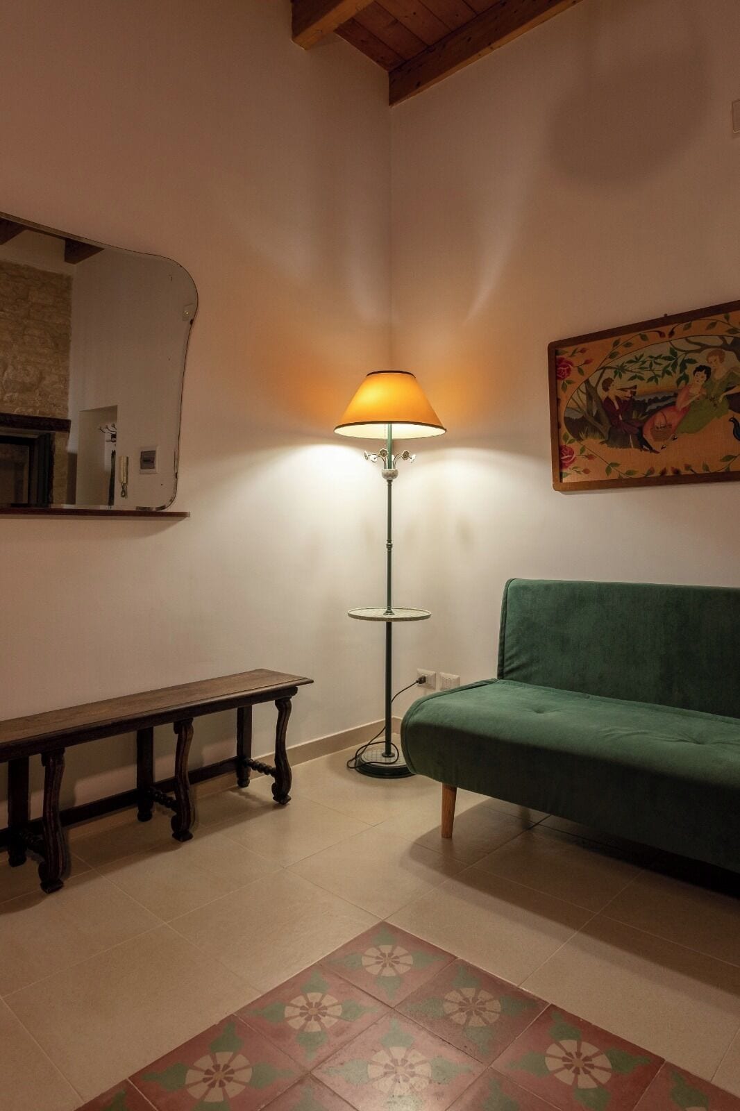 A room with a green sofa, a wooden bench, a floor lamp, and a patterned rug.