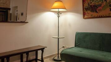 Una habitación con un sofá verde, un banco de madera, una lámpara de pie y un tapete estampado.