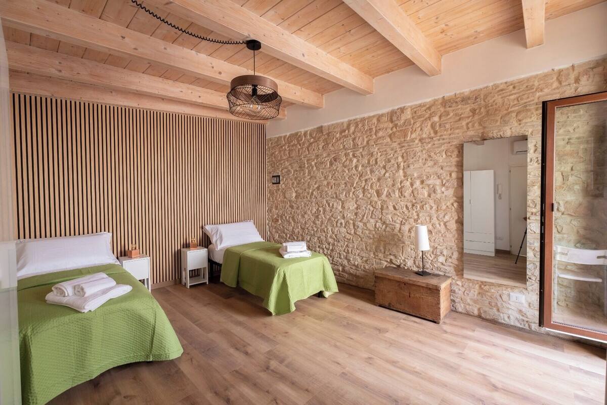 A room with two beds, wooden floors, a stone wall, and a wooden ceiling.