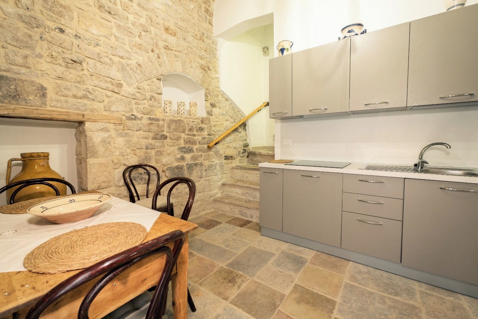 Une cuisine rustique avec des murs en pierre, des chaises en bois, une table avec un saladier et un évier.