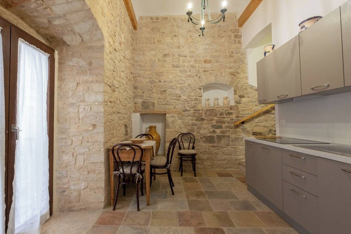 A kitchen with stone walls, a dining table with chairs, and modern cabinetry.