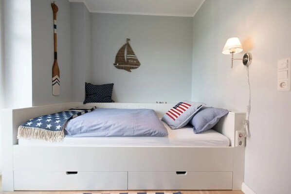 Een keurig opgemaakt bed met een deken met stermotieven, een kussen met stippen en een kussen met rode en witte strepen.