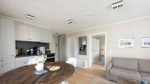 A modern kitchen with white cabinets, a wooden dining table, and a grey sofa in a spacious living area. - Comfortable vacation apartment Meertied in the Lindenhof on Wangerooge with balcony (Wangerooge)