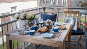 A wooden table with plates of food, cups, and a teapot on a balcony with a railing. - Comfortable vacation apartment Meertied in the Lindenhof on Wangerooge with balcony (Wangerooge)