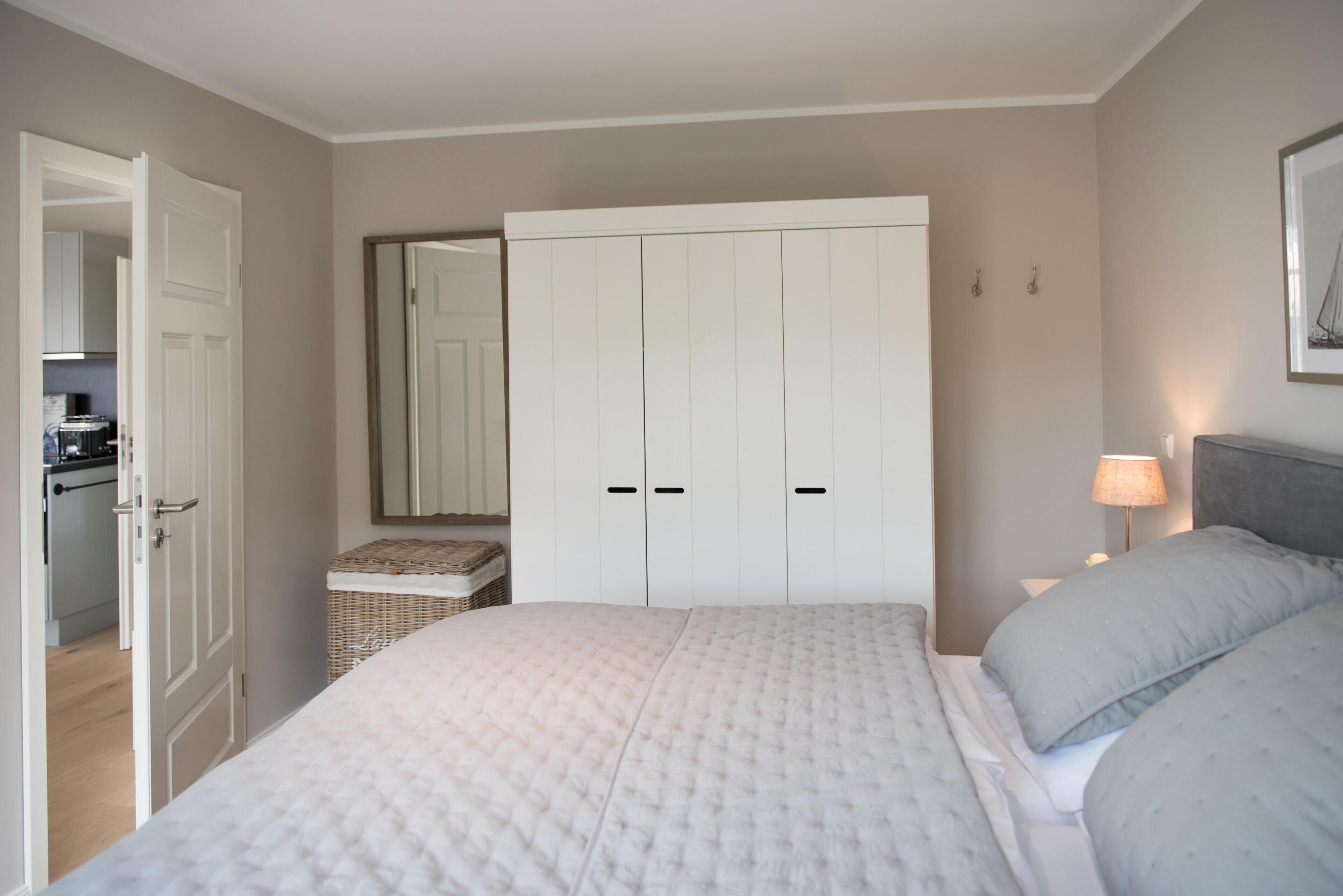 A bedroom with a large bed, a wardrobe, a bedside table with a lamp, and a wicker basket.