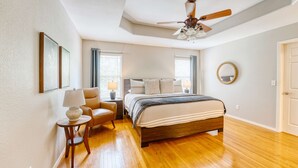 A bedroom with a bed, a chair, a nightstand, a lamp, and a ceiling fan.
