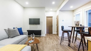 A modern living room with a sofa, coffee table, and a dining area with chairs and a table. - Aurora Lite - Brand new suite with private entrance (Canmore)