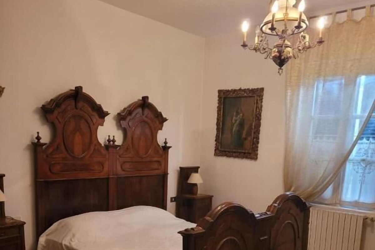 A bedroom with a wooden bed, a chandelier, a radiator, and patterned rugs.