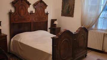 Een slaapkamer met een houten bed, een kroonluchter, een radiator en vloerkleden met een patroon.