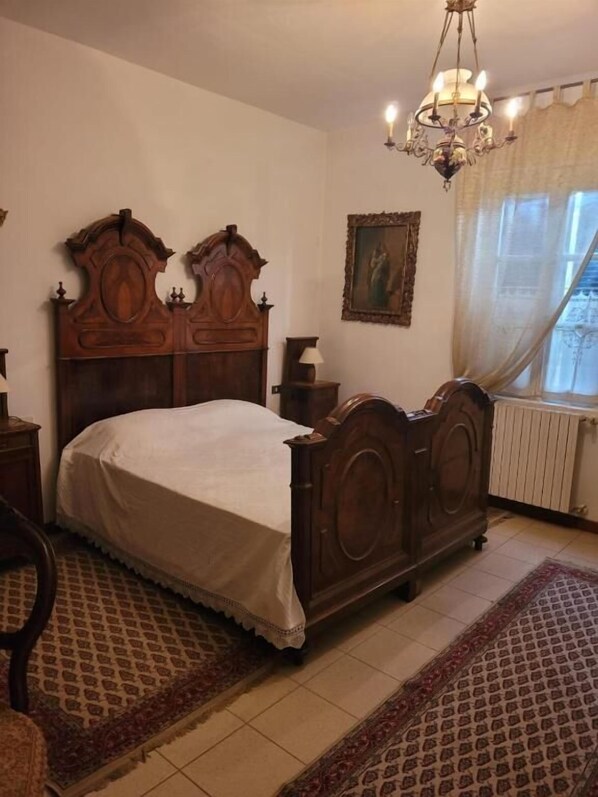 A bedroom with a wooden bed, a chandelier, a radiator, and patterned rugs. - B&B ARCADIA (Casanova Lonati)