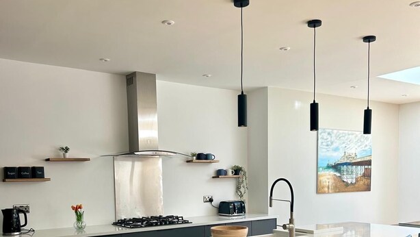 A modern kitchen with a central island, bar stools, pendant lights, and a view of a pier through the window.