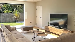 A modern living room with a large sectional sofa, a flat-screen TV, and a dining table.