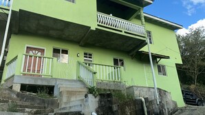 Un edificio a due piani con facciata verde, un balcone con ringhiere bianche e una rampa di scale in cemento che conduce all'ingresso.