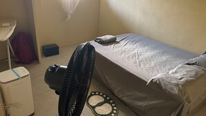 Una stanza piccola e ben illuminata con un letto singolo, un comodino, una ventola e un termosifone.
