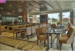 A restaurant with a modern interior, featuring a bar area, multiple dining tables with chairs, and a view of the outdoors.