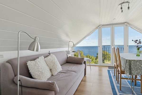 Ein modernes Interieur mit einer Couch, einem Tisch, Stühlen, einem Deckenventilator und Meerblick.