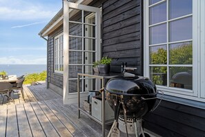 Una terraza de madera con una parrilla, una mesa con sillas y vistas al océano.