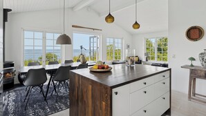 Een moderne keuken met een groot eiland, zwarte stoelen en uitzicht op zee.