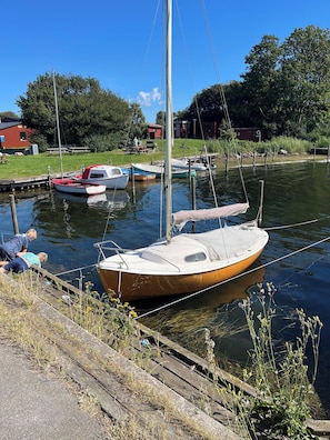 A small boat docked at a pier with a grassy area and a building in the background. - Spacious holiday home on Bogø (Bogø By)