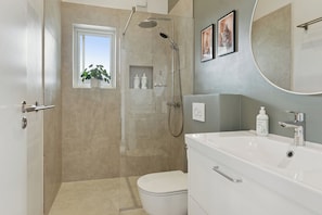 A modern bathroom with a walk-in shower, a toilet, a sink, and a window with a plant. - Spacious holiday home on Bogø (Bogø By)