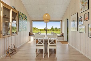 A dining area with a table and chairs, a wicker light fixture, and framed artwork on the walls.
