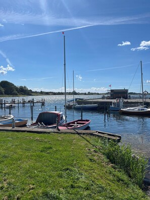 A calm water body with boats docked, a grassy area in the foreground, and a small building with a flag. - Spacious holiday home on Bogø (Bogø By)