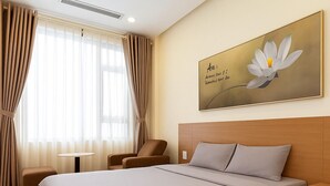 Ein Hotelzimmer mit einem großen Bett, einem Nachttisch, einem Sessel und einem Fenster mit Vorhängen.