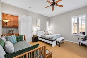 A bedroom with a bed, bedside tables, a lamp, a ceiling fan, and a window with blinds.