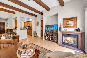 A spacious living room with a fireplace, a television, and a kitchen in the background.
